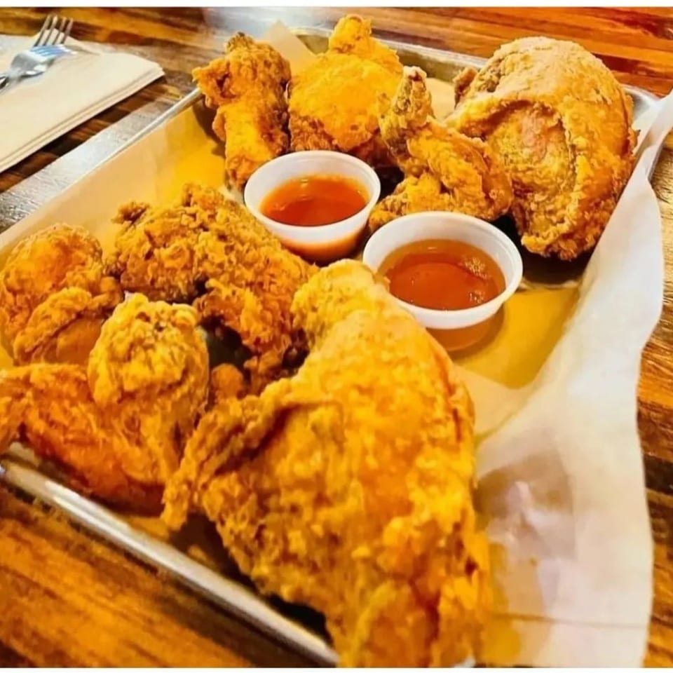 Crispy fried chicken pieces and wings with two small cups of dipping sauce on a metal tray.